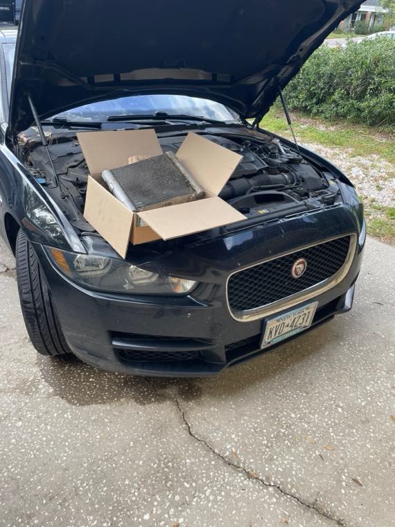 Jaguar XE with hood up and a replacement radiator part boxed on the engine bay